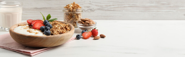 Tasty granola with blueberries, strawberry, yogurt and almonds on white marble table. Banner design with space for text