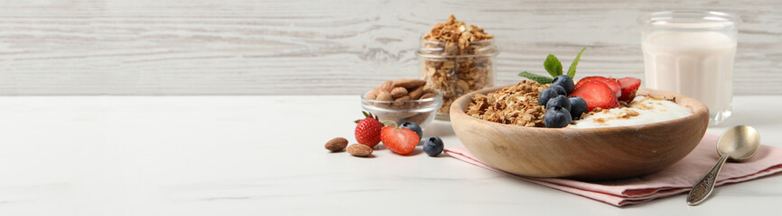 Tasty granola with blueberries, strawberry, yogurt and almonds on white marble table. Banner design with space for text