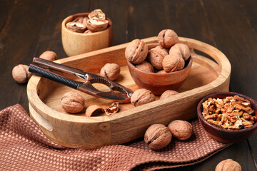 Bowls with walnuts and nutcracker on wooden background