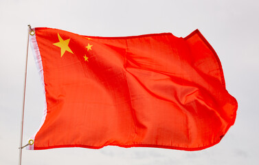 Red flag of China with five golden stars symbolizing Communist Revolution and unity of Chinese people under leadership of CCP waving on flagpole in wind against backdrop of cloudy sky