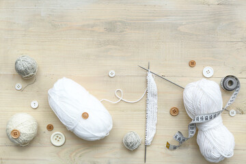 Yarn balls, knitting needles and buttons on light wooden background