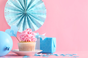 Delicious cupcake with question mark, gift box and decorations on pink background. Gender reveal party concept