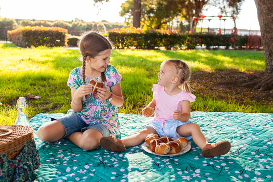 Aussie kids at easter time eating hot cross buns at park on picnic rug smiling together