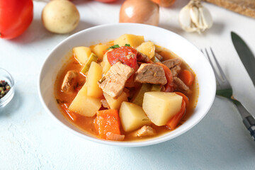 Bowl with delicious beef stew and different ingredients on light blue background