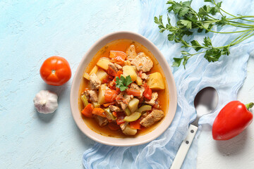 Bowl with delicious beef stew and different ingredients on light blue background