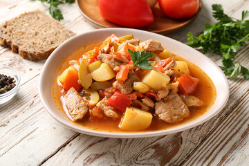 Bowl with delicious beef stew and parsley on white wooden background