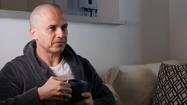 48 year old Brazilian man wearing a robe and drinking a cup of tea and smiling at the camera.
