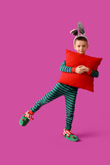Cute little boy in bunny ears with pillow on purple background