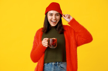 Happy young woman with glass cup of hot mulled wine on yellow background