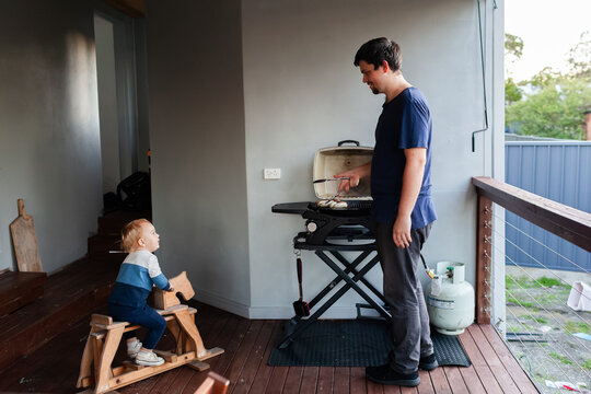 Dad cooking BBQ with toddler boy playing on deck