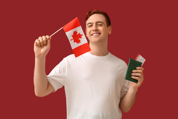 Handsome young happy man with Canadian flag, passport and ticket on red background