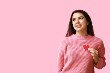 Beautiful young girl with red paper heart on pink background. Valentine's Day celebration