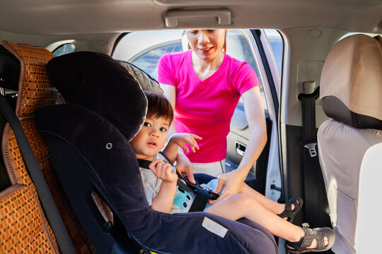 Mum buckling toddler boy into car seat in family car