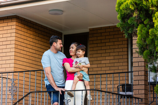 Family of three together on stairs at front of brick home looking at each other