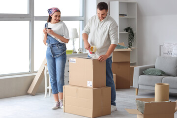 Happy young couple taping box in room on moving day