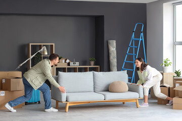 Happy young couple carrying sofa in room on moving day