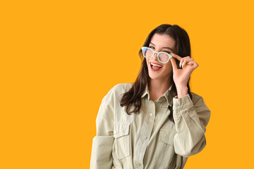 Happy smiling young woman in eyeglasses winking on yellow background