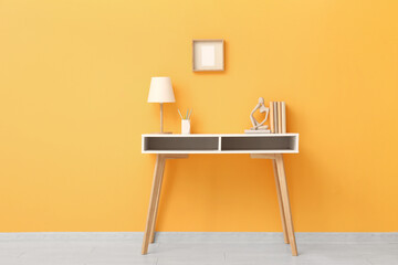Stylish workplace with lamp and desk near yellow wall