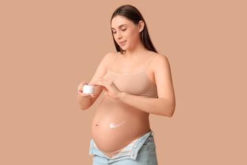 Young pregnant woman applying cream against stretch marks on beige background