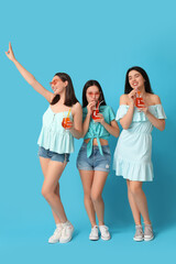 Obraz premium Beautiful young women with glasses of cocktail on blue background. Summer party