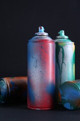 Many spray paint cans with caps on dark background