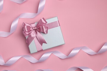 Beautiful gift box with color bow and ribbons on pink background, flat lay