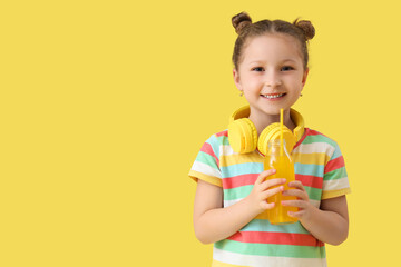 Cute little girl with bottle of lemonade on yellow background