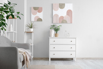 Grey sofa, shelving units, houseplants and beautiful pictures on white wall in living room