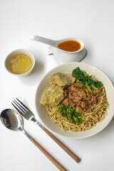 Mie Ayam Pangsit (Noodles with Chicken, Dumplings and vegetables ) is Indonesian popular food. Served in bowl on white table. Selective focus.