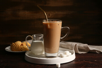 Glass cup of iced latte and plate with sweet cookies on wooden background