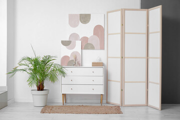 Stylish room with chest of drawers, houseplant and picture on white wall