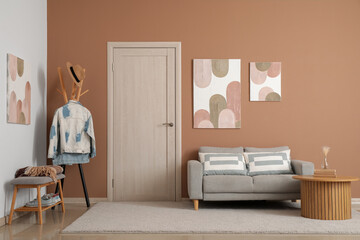 Interior of modern living room with grey sofa, coat rack and stylish pictures hanging on beige wall