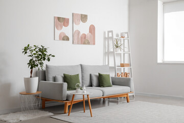 Interior of stylish living room with comfortable sofa, shelving unit, coffee table and pictures on white wall