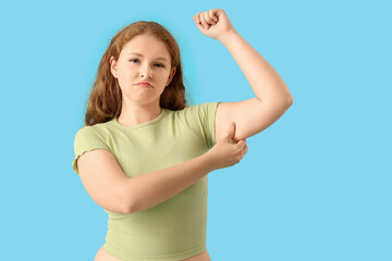 Fototapeta premium Sad young woman with chubby arms on blue background. Weight gain concept