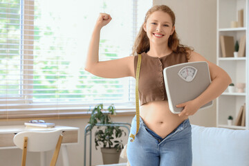 Happy young woman in tight jeans with scales at home. Weight gain concept