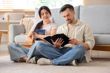 Religious couple reading Holy Bible on floor at home