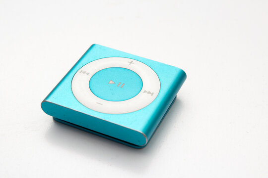 Saint-Petersburg, Russia - May 10, 2022: Blue small metal square old music player iPod Shuffle with big round button on white background close up. Concept of vintage, technique, technology, sing, song