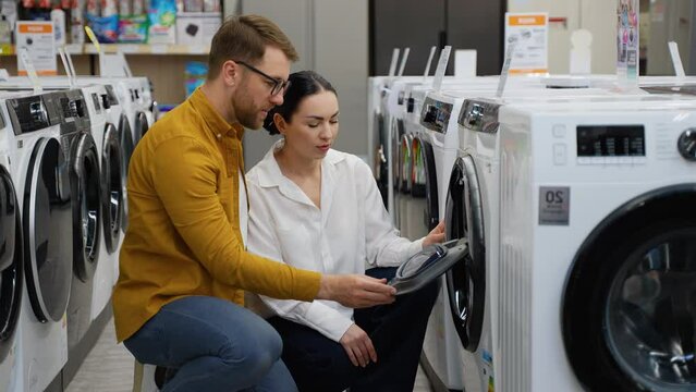 Just married couple chooses a smart washing machine in a consumer electronics store for new home