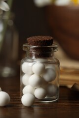 Homeopathy. Pills in glass bottle on wooden table, closeup