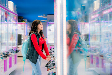 Young Latina woman smiling and playing arcade games in Akihabara, Tokyo, Japan, surrounded by...
