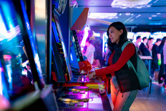 A young Latina woman smiling while playing arcade games in Akihabara, Tokyo, Japan, with glowing futuristic screens.