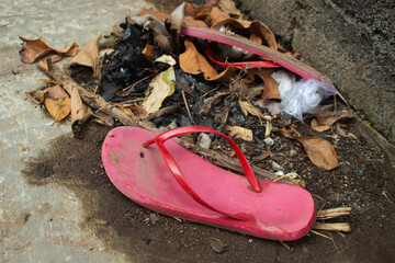 Broken flip-flop on trash. Old damaged red sandal is thrown in the trash.