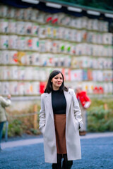 Fototapeta premium A young Latina woman standing in front of decorative sake barrels at Meiji Shrine in Tokyo, Japan, looking content.