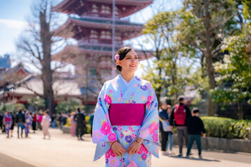 Fototapeta premium Young Latina woman in a colorful kimono smiling at the grounds of Sensoji Temple in Asakusa, Tokyo, Japan, surrounded by traditional architecture.