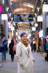 Young Latina woman in a white coat exploring the bustling Nakamise Shopping Street at night in Asakusa, Tokyo, Japan.
