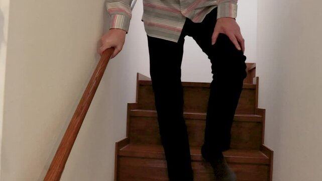 膝を押さえながらゆっくりと階段を下りる男性
