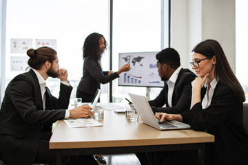 Group of business professionals in team meeting discussing charts and graphs with presentation in modern office setting. Collaboration scene with employees focused on strategy and data analysis.