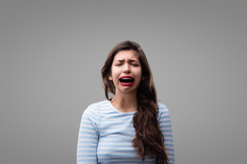 Young woman crying desperately on a grey background