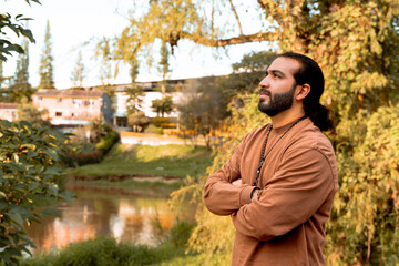 Latin man with long bearded hair and brown jacket, enjoying the golden hour in his country, trees and nature. Holidays and peace and quiet.