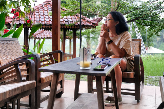 A woman sitting alone in a wooden chair, hands supporting her chin; serious expression